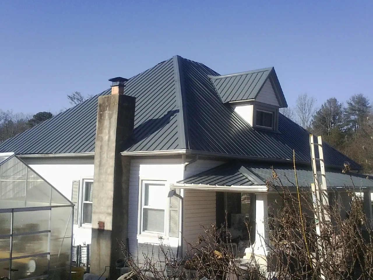 Dark blue standing seam metal roof on a white farmhouse with dormer — Slate & Tile Roof Repair by Roofing Brothers in Rivesville
