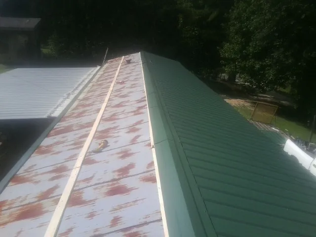 Old rusted panels beside newly installed green metal roofing — Wind Damage Roof Repair by Roofing Brothers in Rivesville