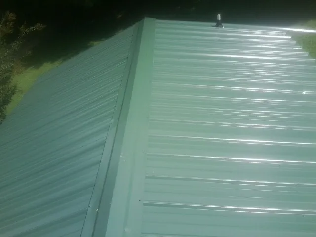 New green metal panels meeting at the ridge of a roof — Flat Roof Repair work by our crew in Rivesville