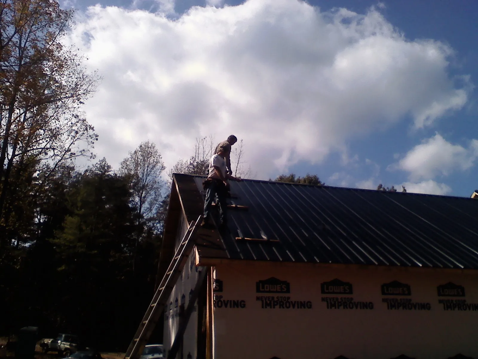 Roofer fastening dark metal panels high against a cloudy sky, from a Roof Inspection job in Rivesville