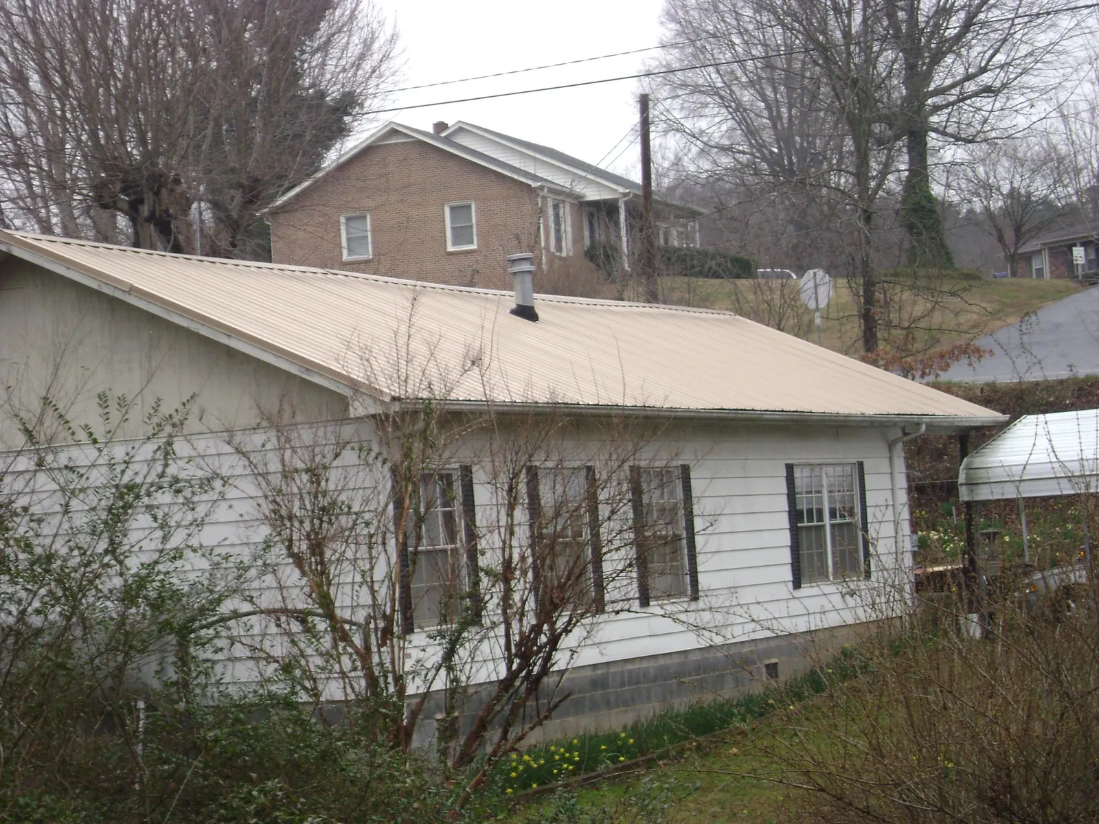 Tan metal roof on a white sided house set into a hillside — Commercial Roofing by Roofing Brothers in Rivesville